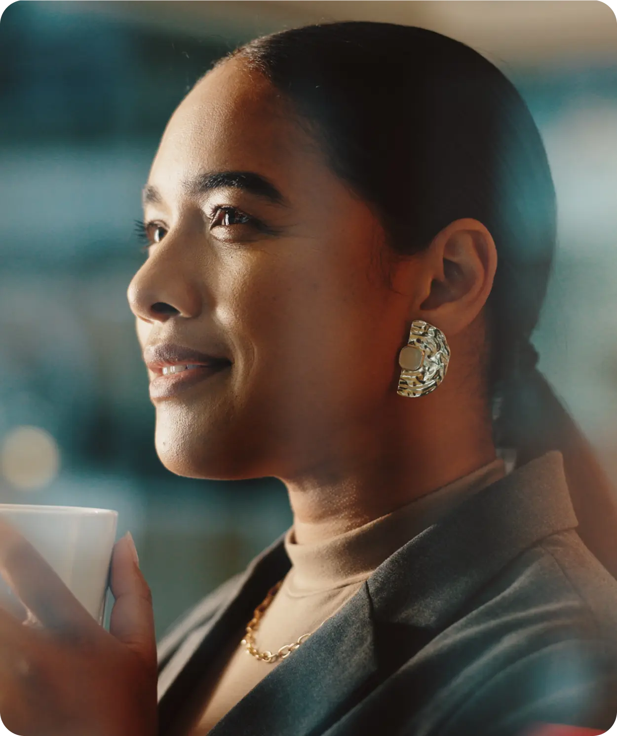 Woman drinking from coffee cup wearing green suit and earrings.